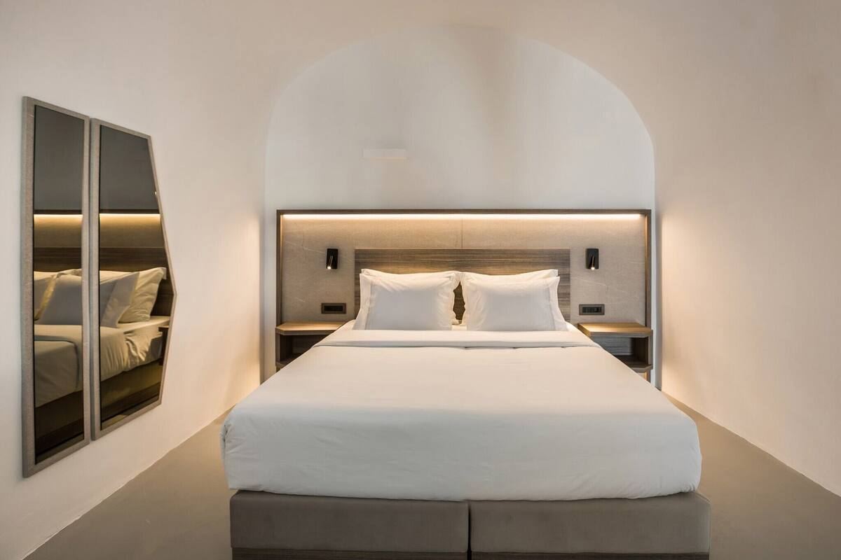Une chambre d’hôtel moderne avec un grand lit, un banc intégré au pied du lit et un miroir au mur.