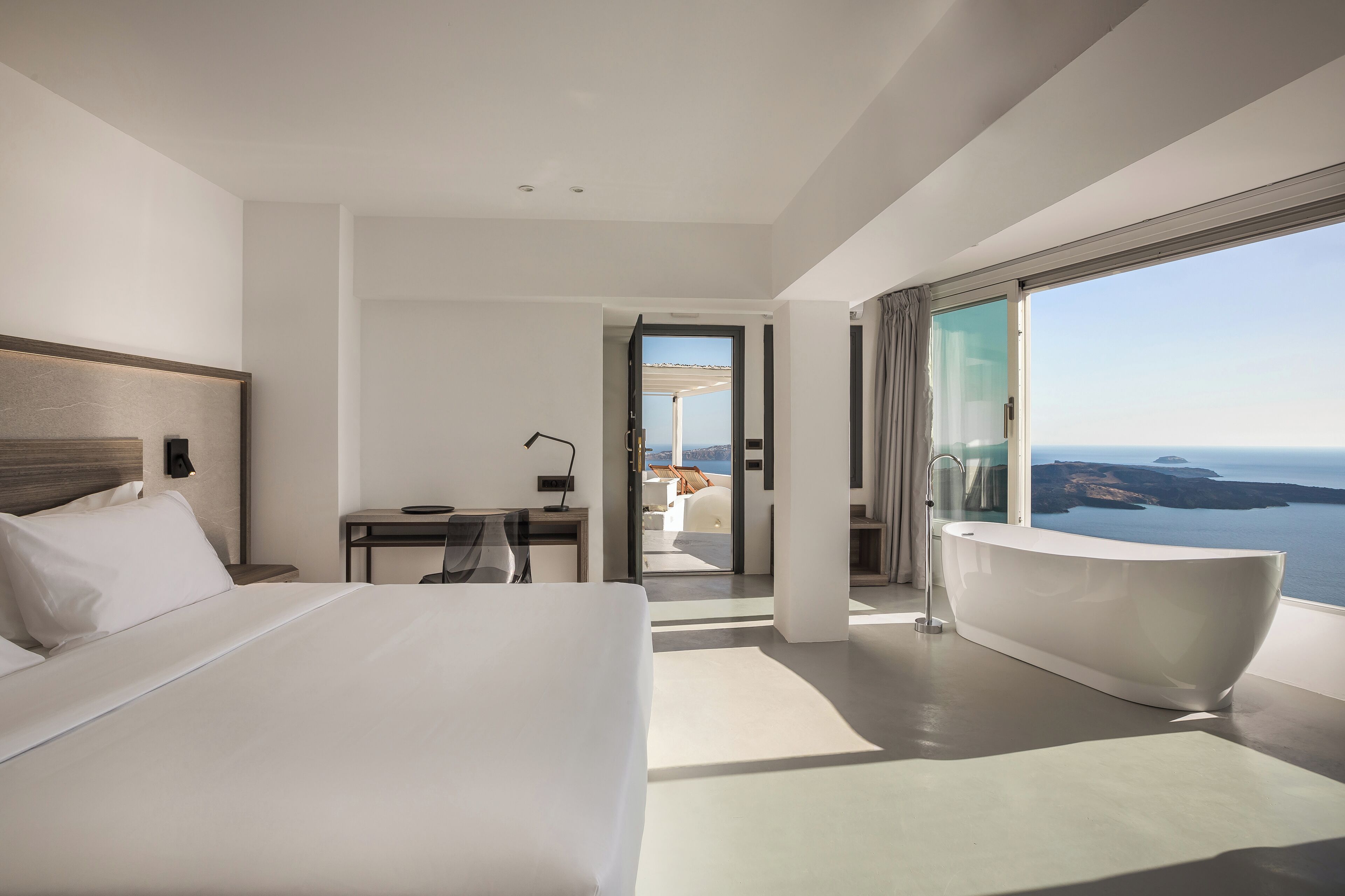 Habitación de hotel moderna con una cama grande, un escritorio, una bañera y un balcón con vistas al mar.