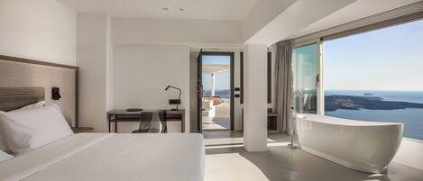 A modern hotel room with a large bed, a desk, a bathtub, and a balcony with a view of the sea.