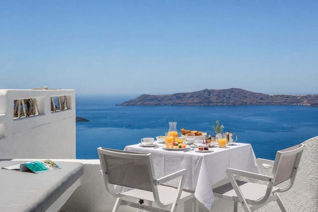 Ein Esstisch, gedeckt für das Frühstück, mit Blick auf das Meer und eine entfernte Insel.