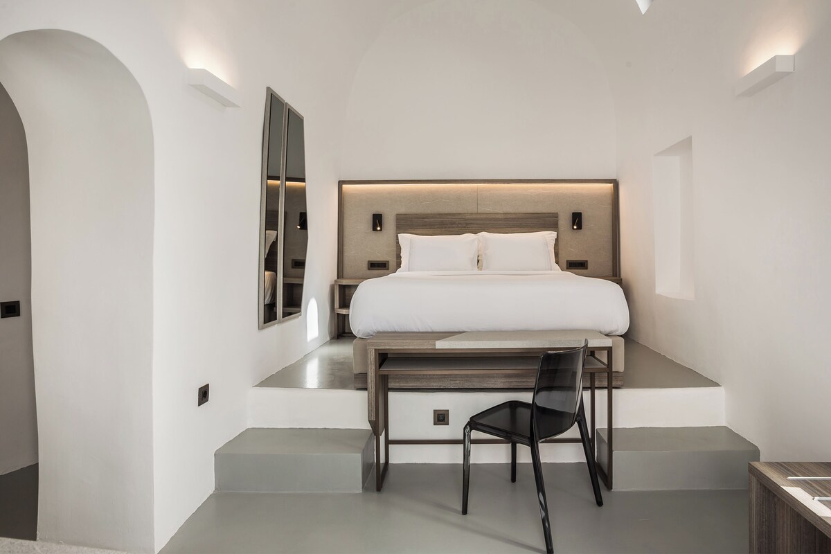 A modern bedroom with a bed, bedside table, chair, and built-in shelving.