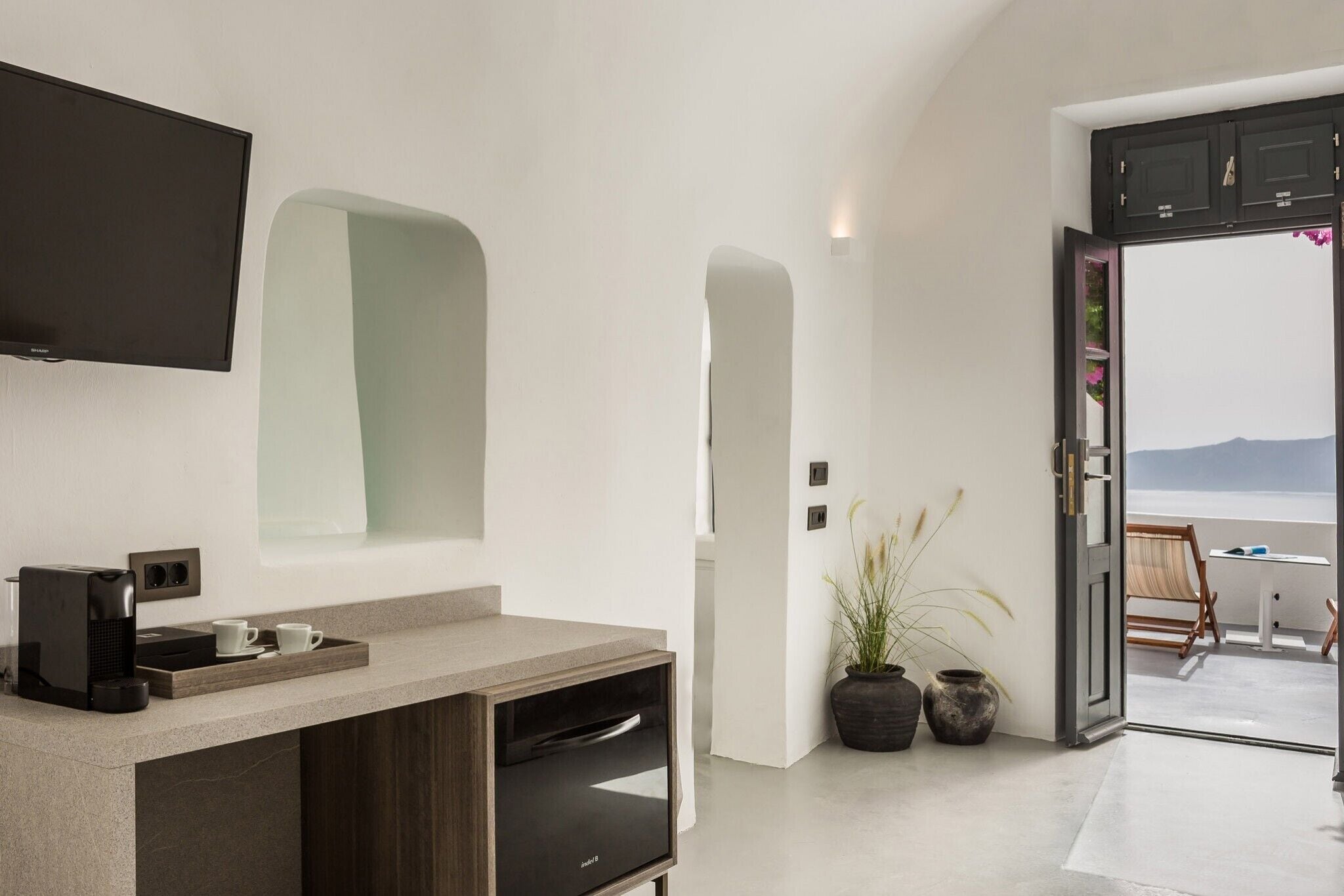 A modern kitchen with a built-in dishwasher, a coffee machine, and a large window overlooking a balcony with a view of the sea.
