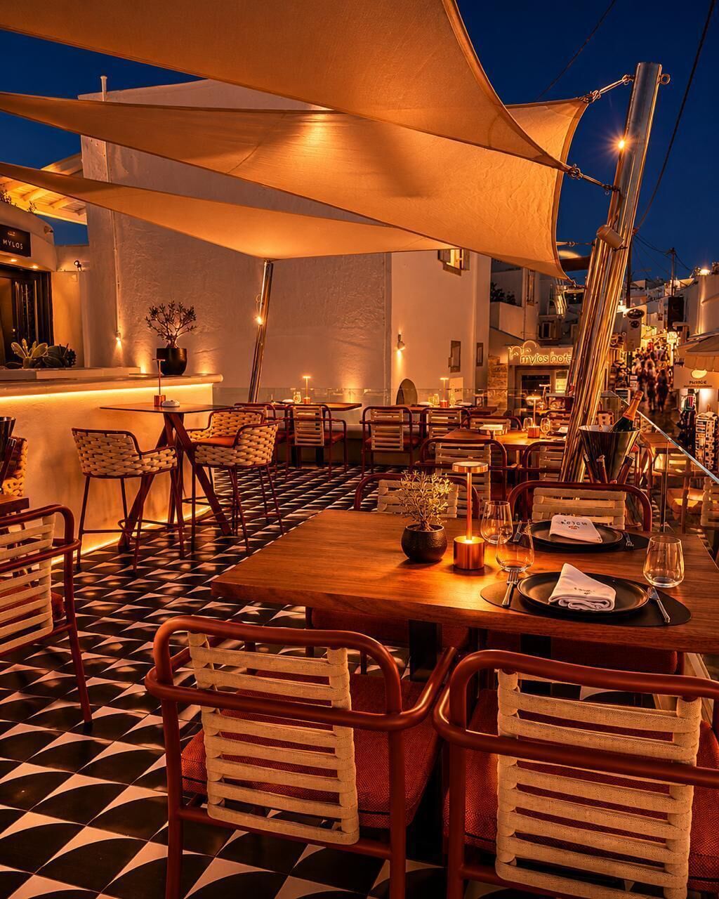 An outdoor dining area with tables and chairs, a bar, and a view of the city at night.
