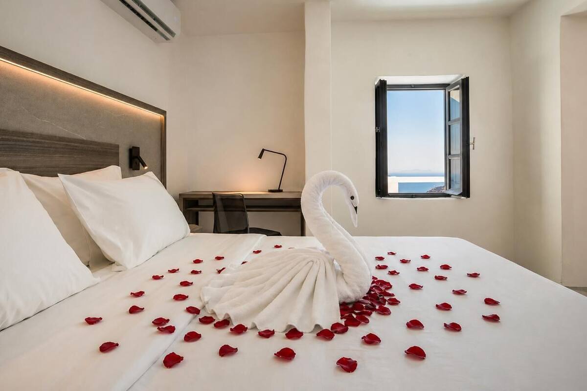 Une chambre d’hôtel avec un lit, un bureau, une chaise, une fenêtre donnant sur un beau paysage et un objet décoratif en forme de cygne posé sur le lit.
