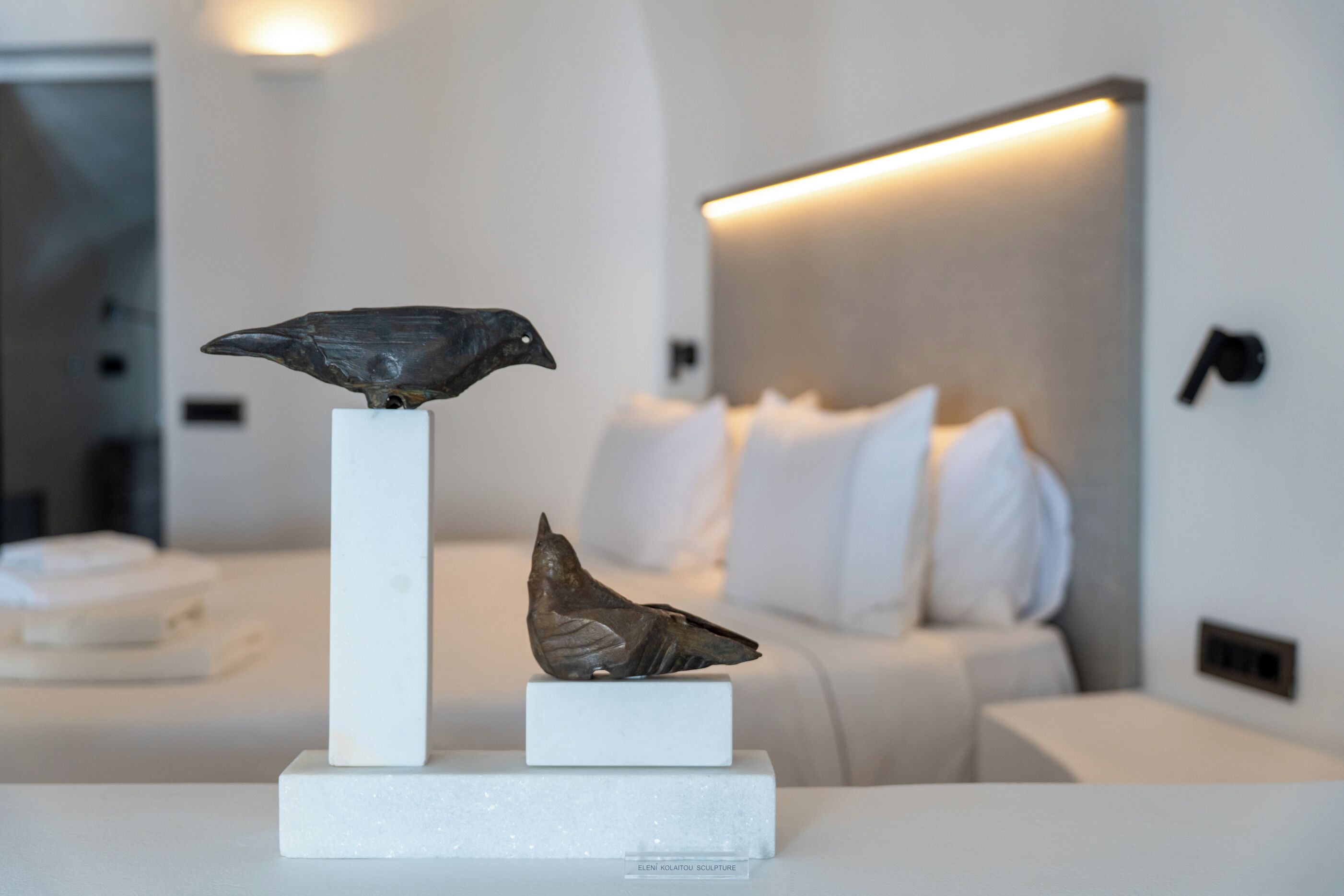 Een moderne kamer met een wit bed, een witte nachtkastje en een sculptuur van een vogel op het nachtkastje.
