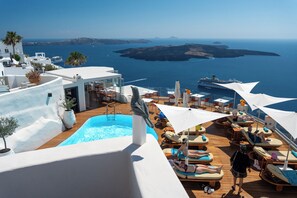 Ein Poolbereich mit Liegestühlen und Sonnenschirmen, ein Pool und Blick auf das Meer und Inseln.