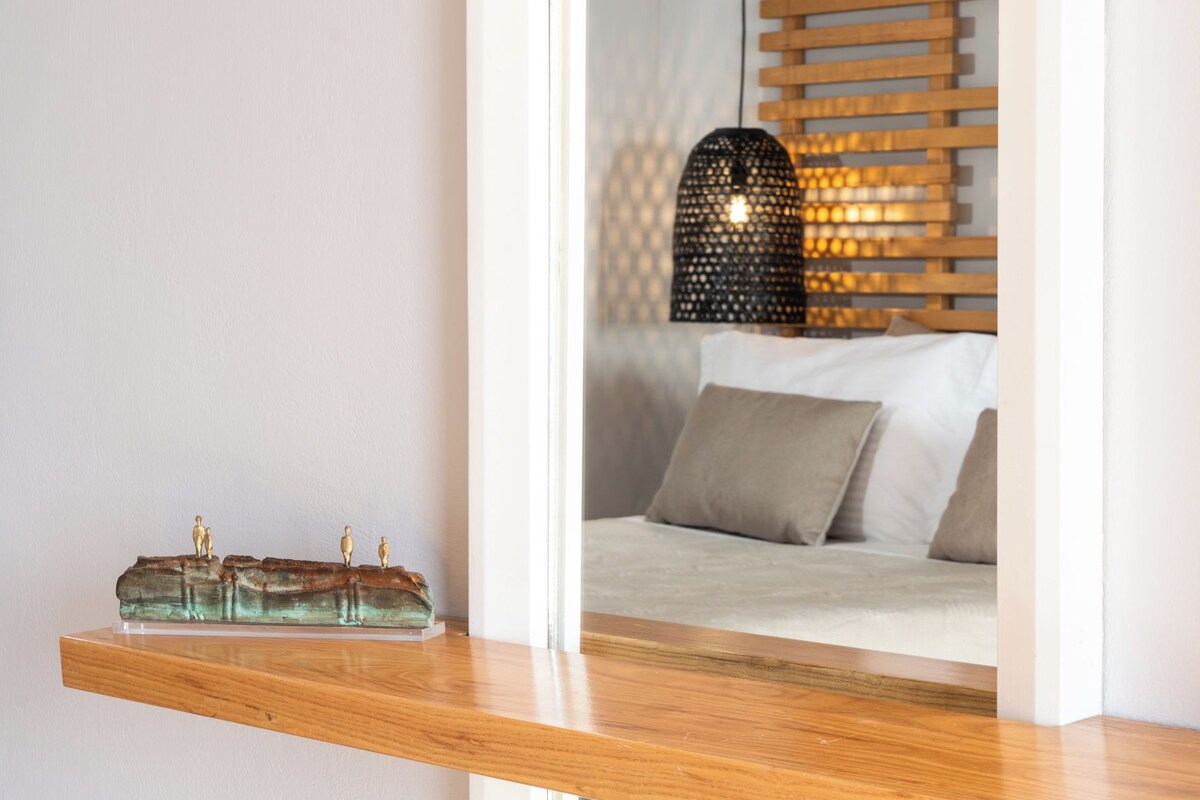 A modern room with a wooden shelf, a bed with pillows, a hanging light fixture, and a patterned wall.