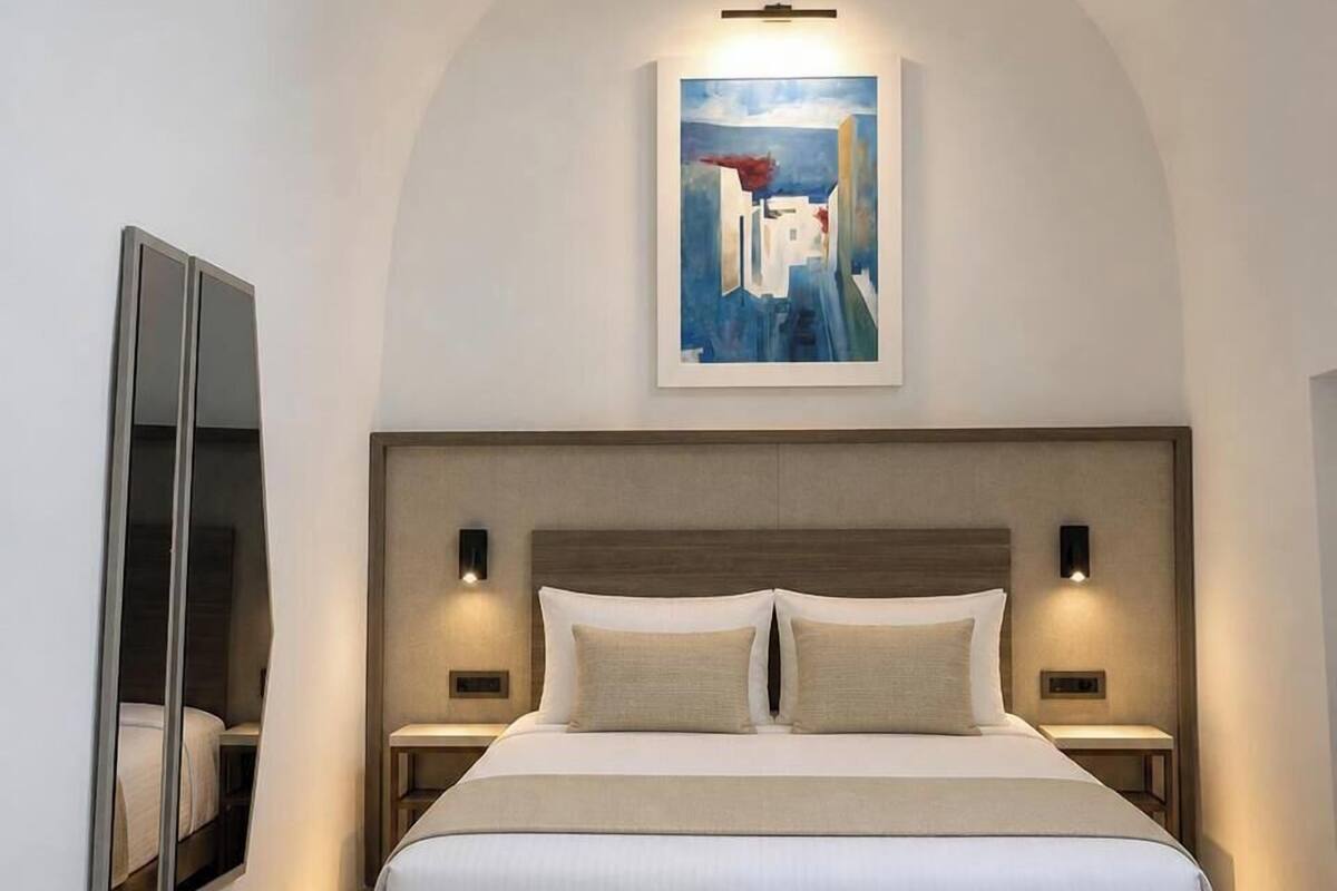 Une chambre d’hôtel moderne dotée d’un grand lit, de deux tables de chevet, d’une œuvre d’art accrochée au mur et d’une banquette intégrée au pied du lit.