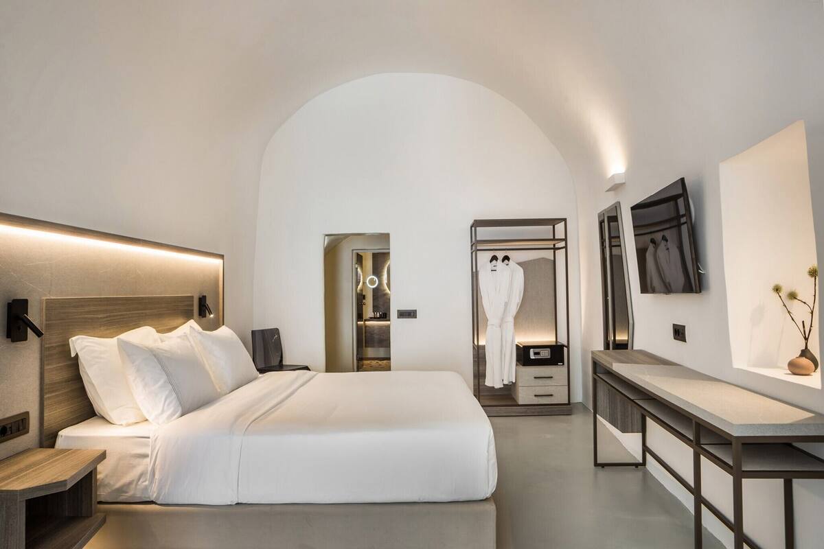Une chambre d’hôtel moderne dotée d’un grand lit, de tables de chevet, d’un bureau et d’un téléviseur fixé au mur.