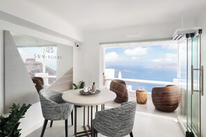 Un intérieur moderne avec une table ronde, deux chaises, une vue sur la mer et un panneau indiquant « SUN ROCKS ».
