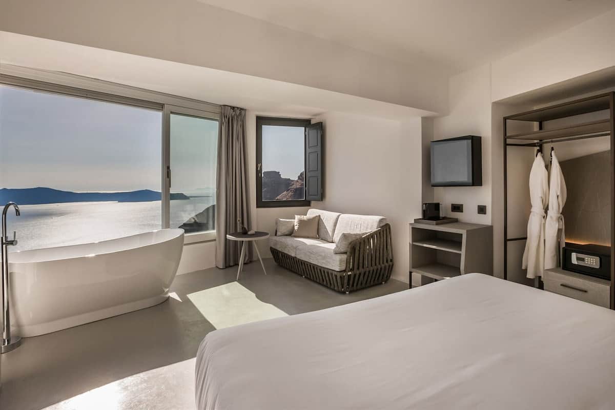 Une chambre d’hôtel moderne dotée d’une grande baignoire, d’un canapé, d’une télévision et offrant une vue sur la mer.