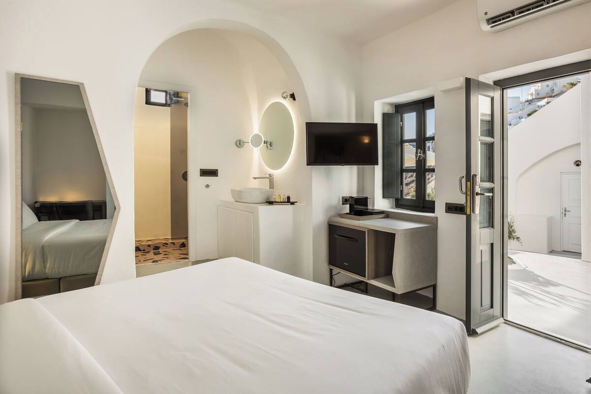Une chambre d’hôtel moderne équipée d’un lit, d’un bureau avec un ordinateur, d’une télévision et d’une salle de bain avec un miroir et un lavabo.