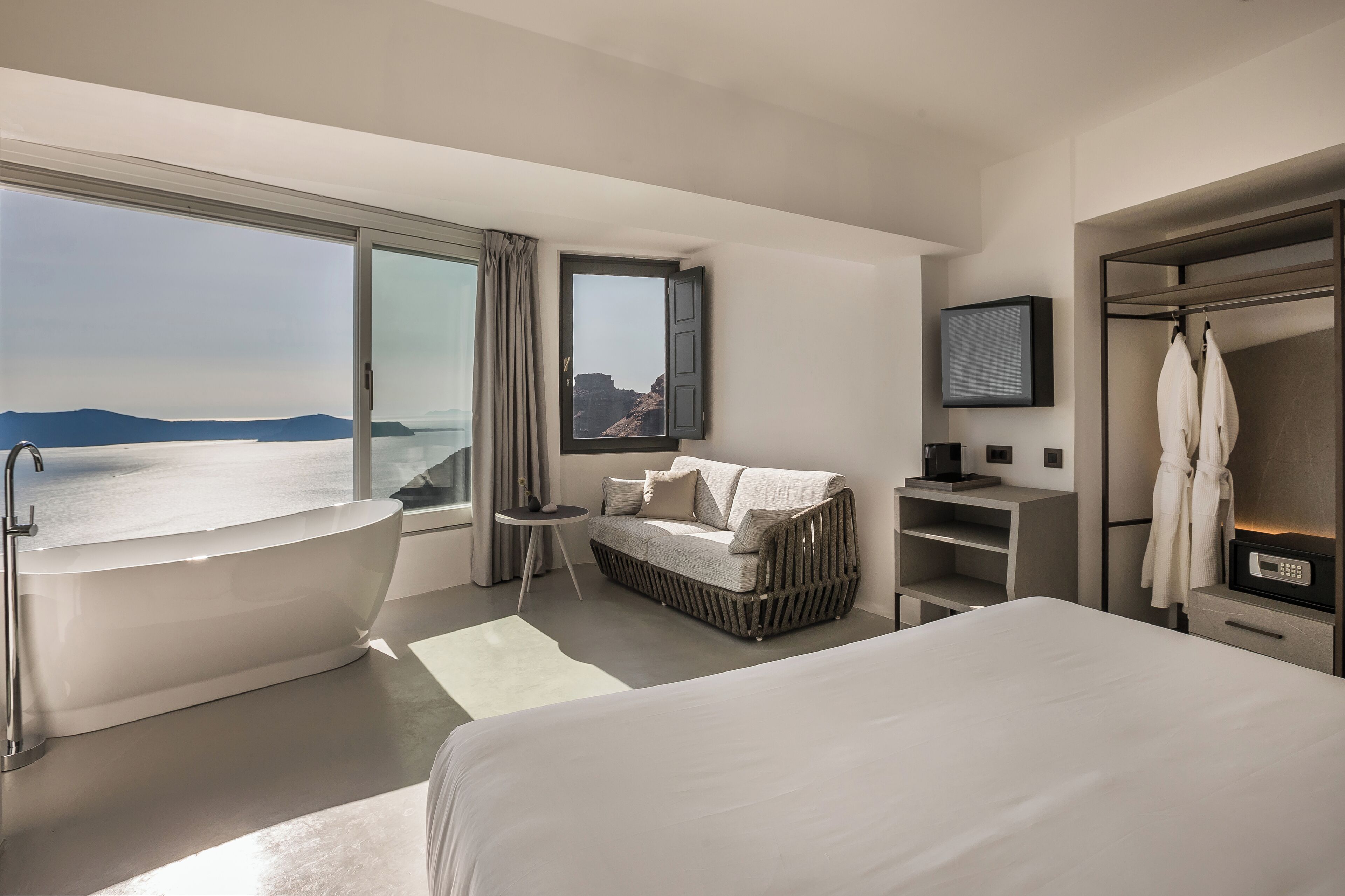 Une chambre d’hôtel moderne dotée d’un grand lit, d’une baignoire, d’un canapé, d’une télévision et offrant une vue sur la mer.