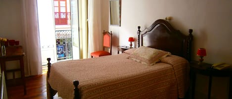 Un dormitorio con una cama de madera, una mesita de noche con lámpara, una silla y una ventana con cortinas.