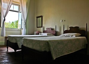 A room with two beds, a window with curtains, a mirror, and a bedside table with a lamp. - Residencial União (Tomar)