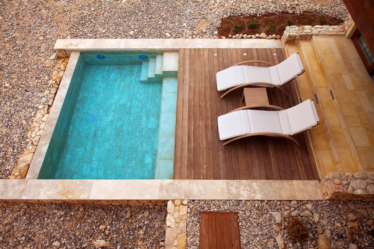 Uma piscina pequena com deck de madeira e espreguiçadeiras.