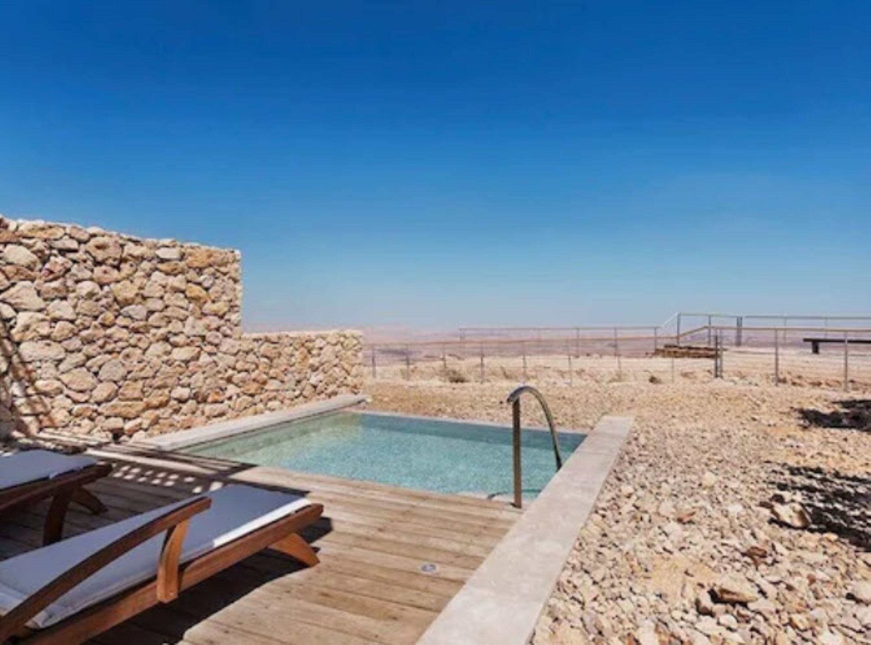Un espace piscine agrémenté d’un mur en pierre, d’une terrasse en bois et de chaises longues.