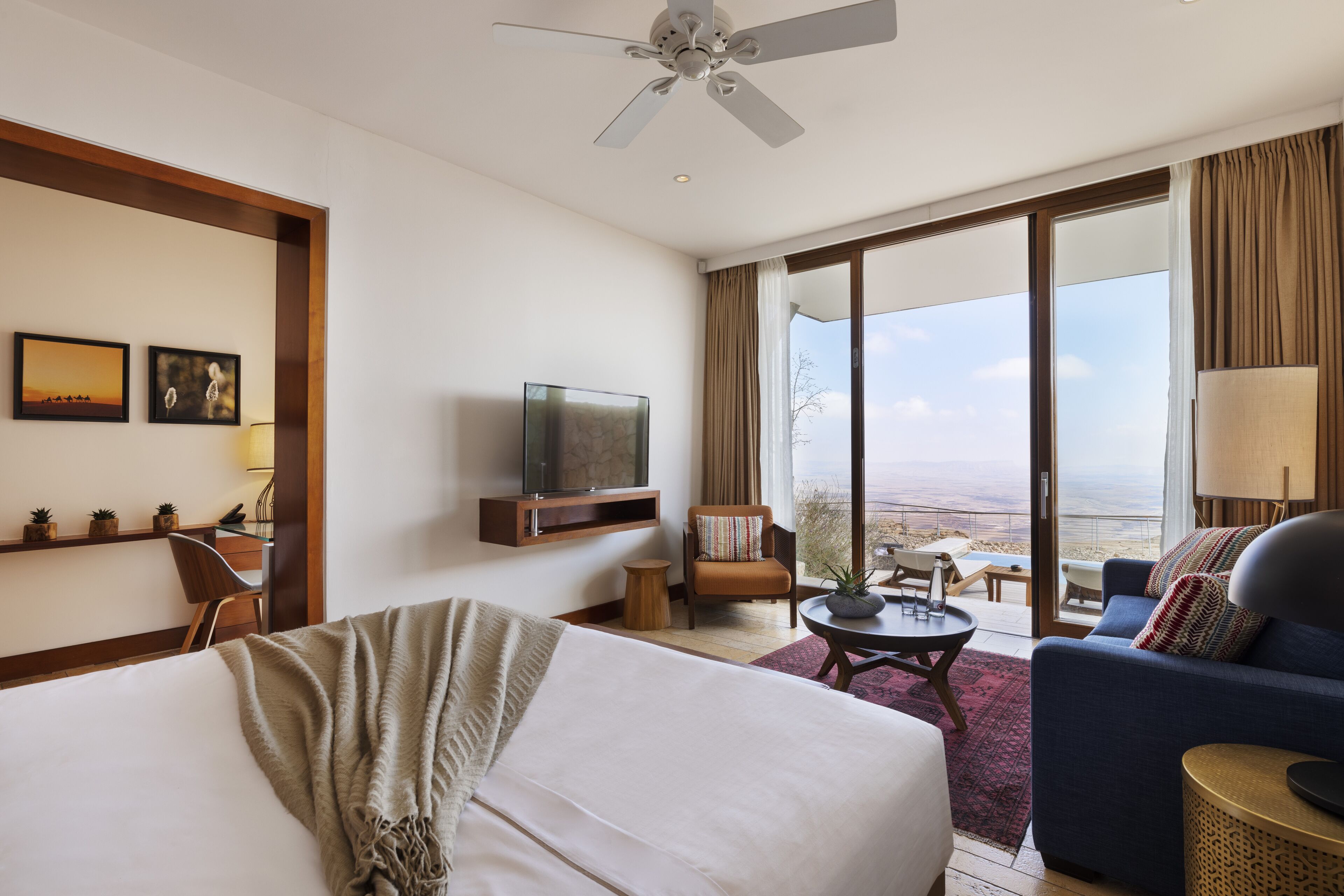 A hotel room with a bed, a sofa, a TV, a chair, a small table, and a large window offering a view of the outdoors.