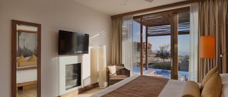 A hotel room with a large bed, a flat-screen TV, a fireplace, a balcony with a view of the landscape, and a ceiling fan.