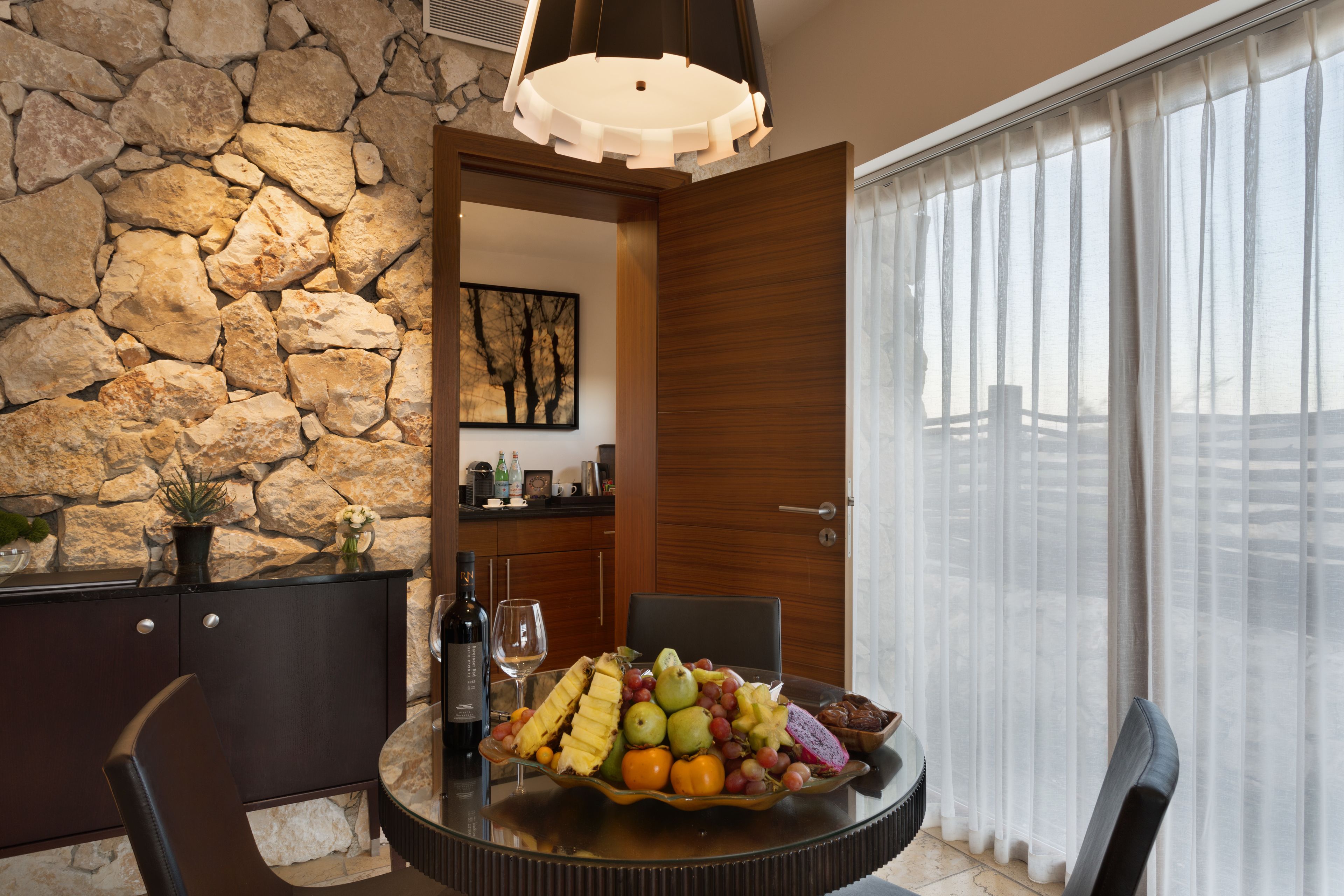 A dining area with a stone wall, a wooden door, and a view through sheer curtains.