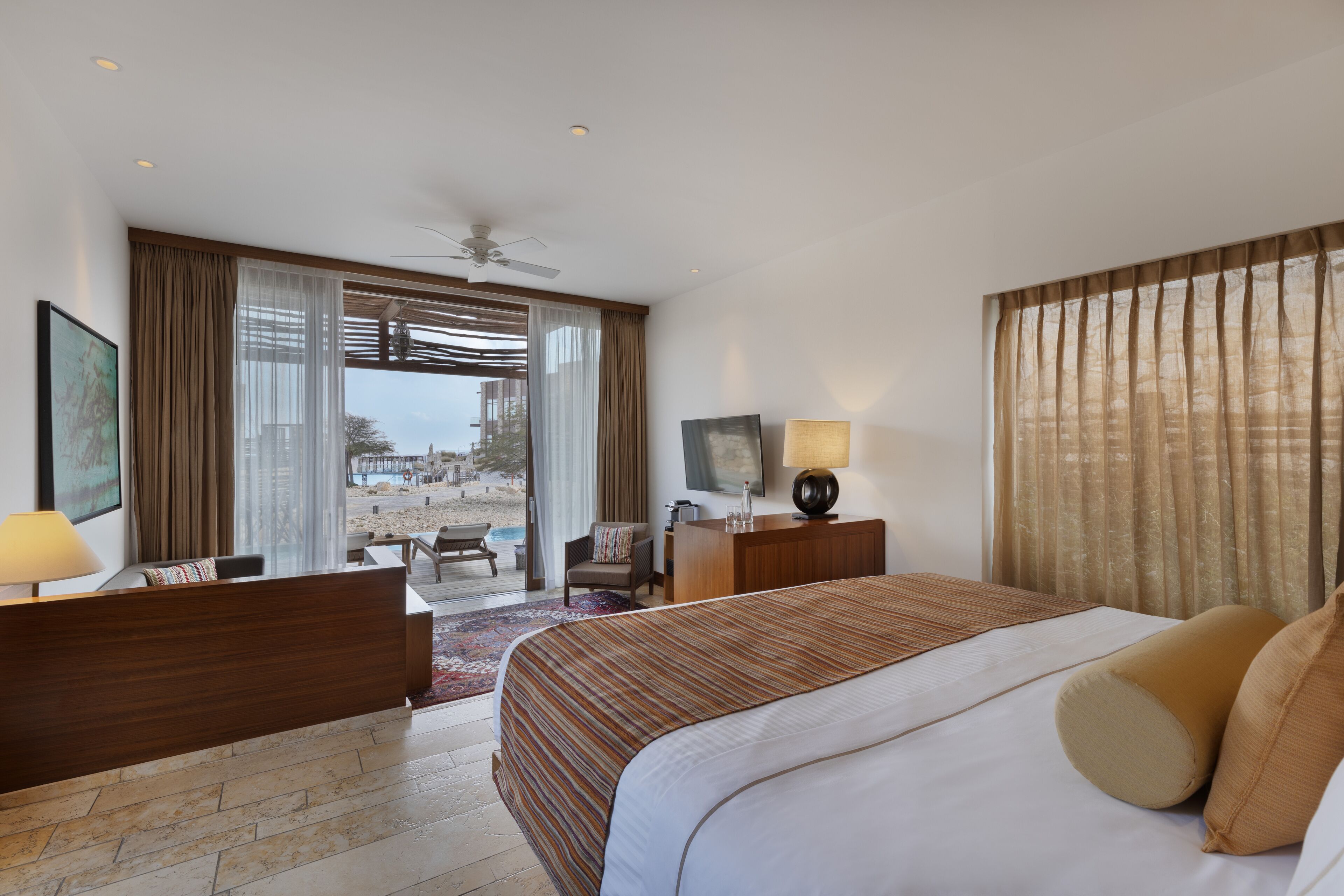 Una habitación de hotel con cama, escritorio, silla, televisor y ventana con cortinas.