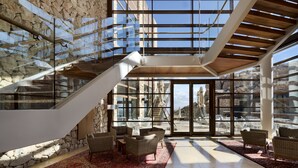 A spacious indoor area with a stone wall, a staircase, and wicker furniture. - Beresheet by Isrotel exclusive (Ramat Negev)