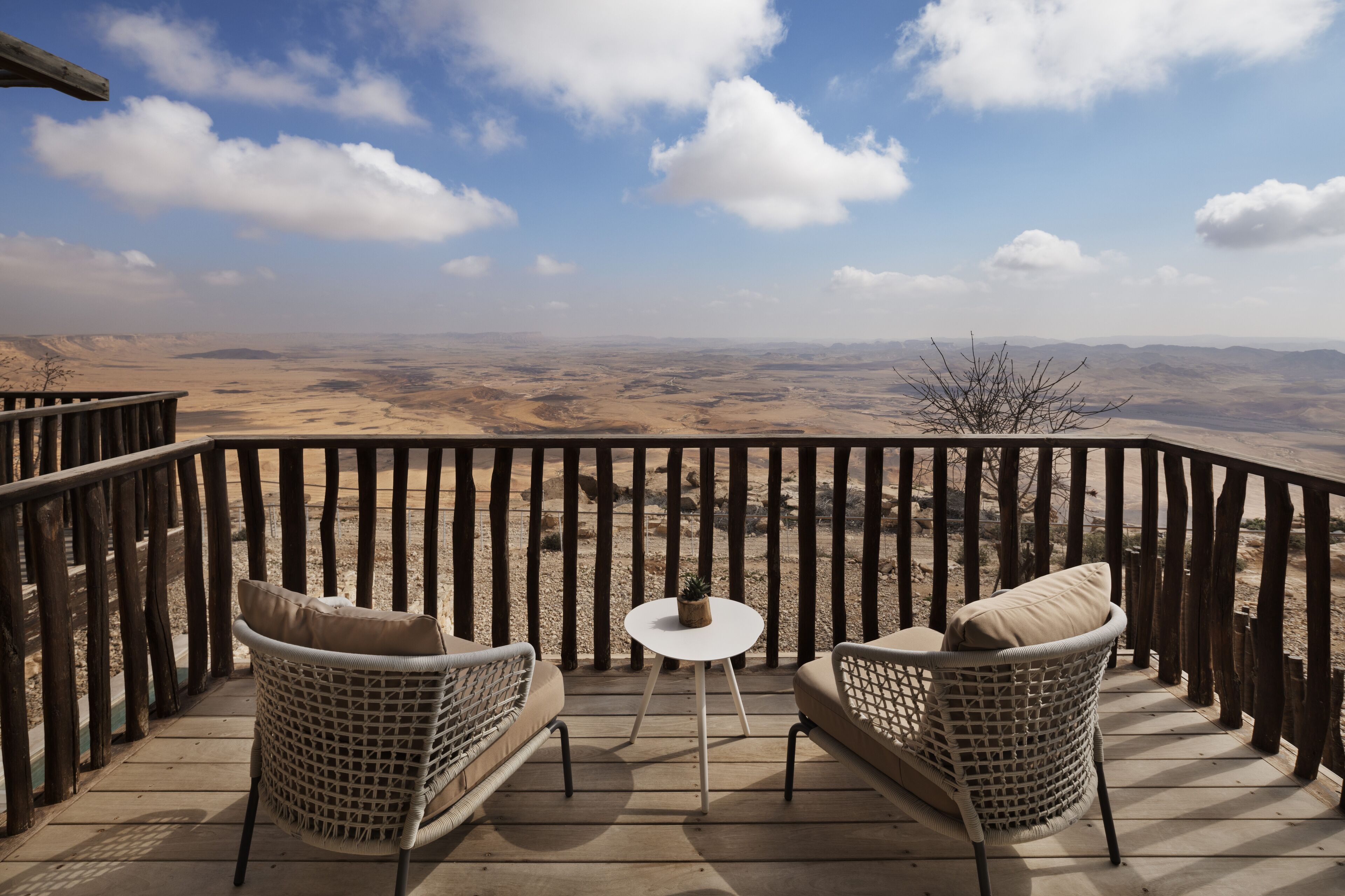 A balcony with wicker furniture and a small table, overlooking a vast desert landscape.