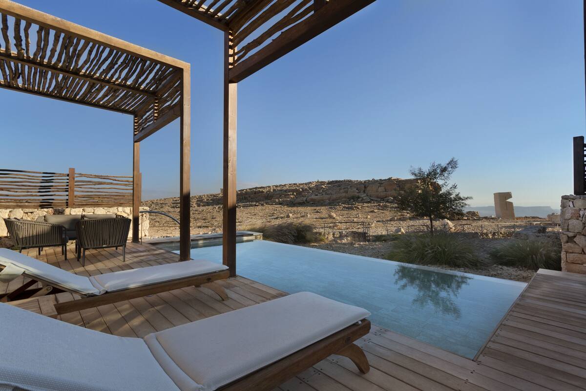 Um deck de madeira com cadeiras de descanso e piscina, com vista para uma paisagem rochosa.