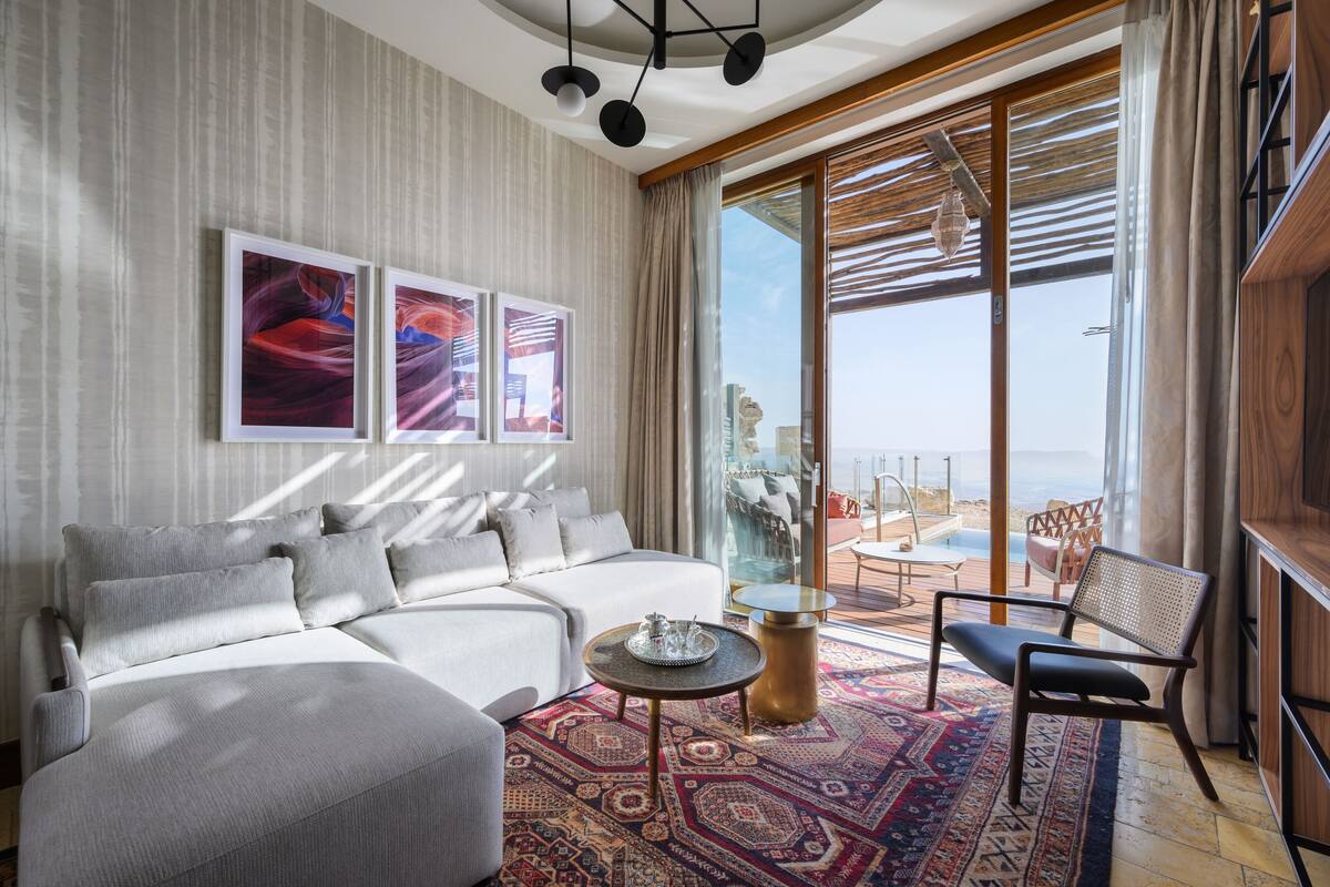 Uma sala de estar moderna com sofá, mesa de centro e vista para o oceano através de grandes janelas.