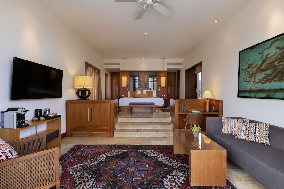 Quarto de hotel moderno com televisão de tela plana, sofá, mesa de centro, escrivaninha e cama com vista para a cidade.
