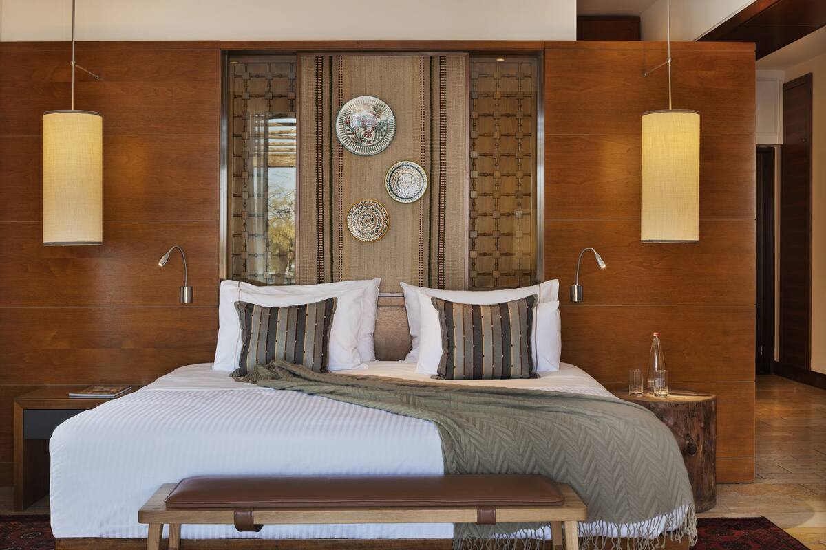 Quarto moderno com cama grande, cabeceira de madeira e pratos decorativos na parede.