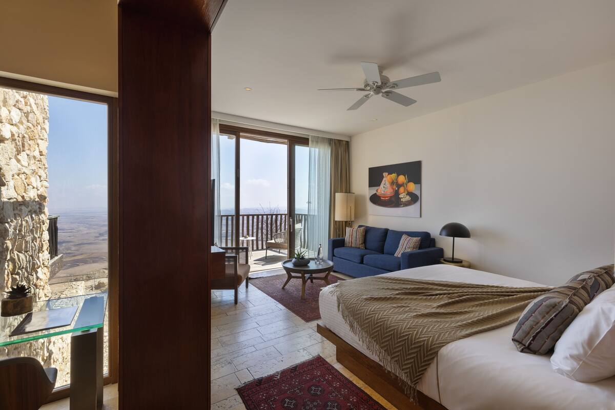 Quarto com cama grande, varanda com vista, sofá e mesa de jantar.