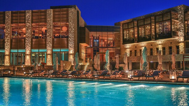A hotel with a swimming pool, lounge chairs, and a stone facade. - Beresheet by Isrotel exclusive (Ramat Negev)
