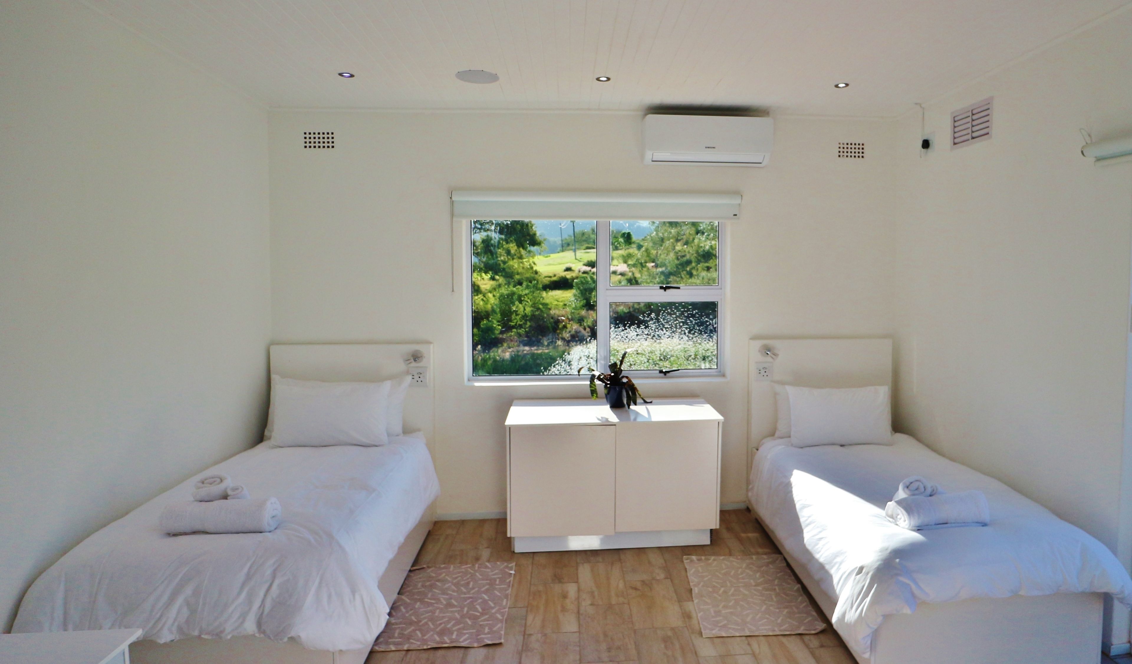 Una camera da letto con due letti singoli, un piccolo comò bianco, una finestra con vista sul verde e un condizionatore d'aria a parete.