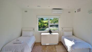 Una camera da letto con due letti singoli, un piccolo comò bianco, una finestra con vista sul verde e un condizionatore d'aria a parete.