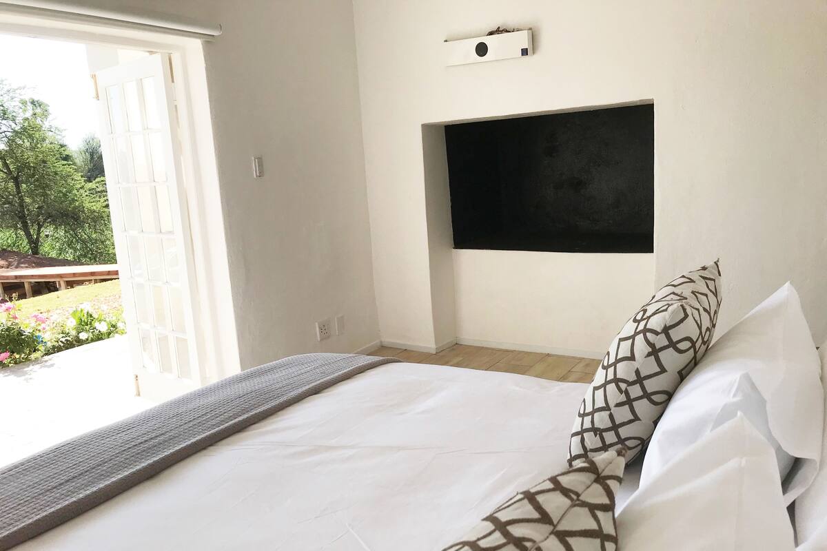 A bedroom with a bed, a TV mounted on the wall, and a view of the outdoors.