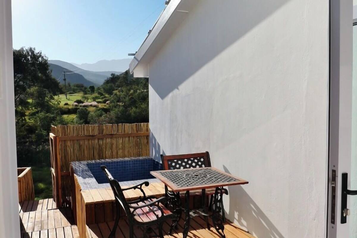 A wooden deck with a table and chairs, a view of a mountainous landscape, and a white wall.