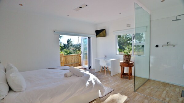 A modern bedroom with a large bed, a desk, and a glass shower enclosure.