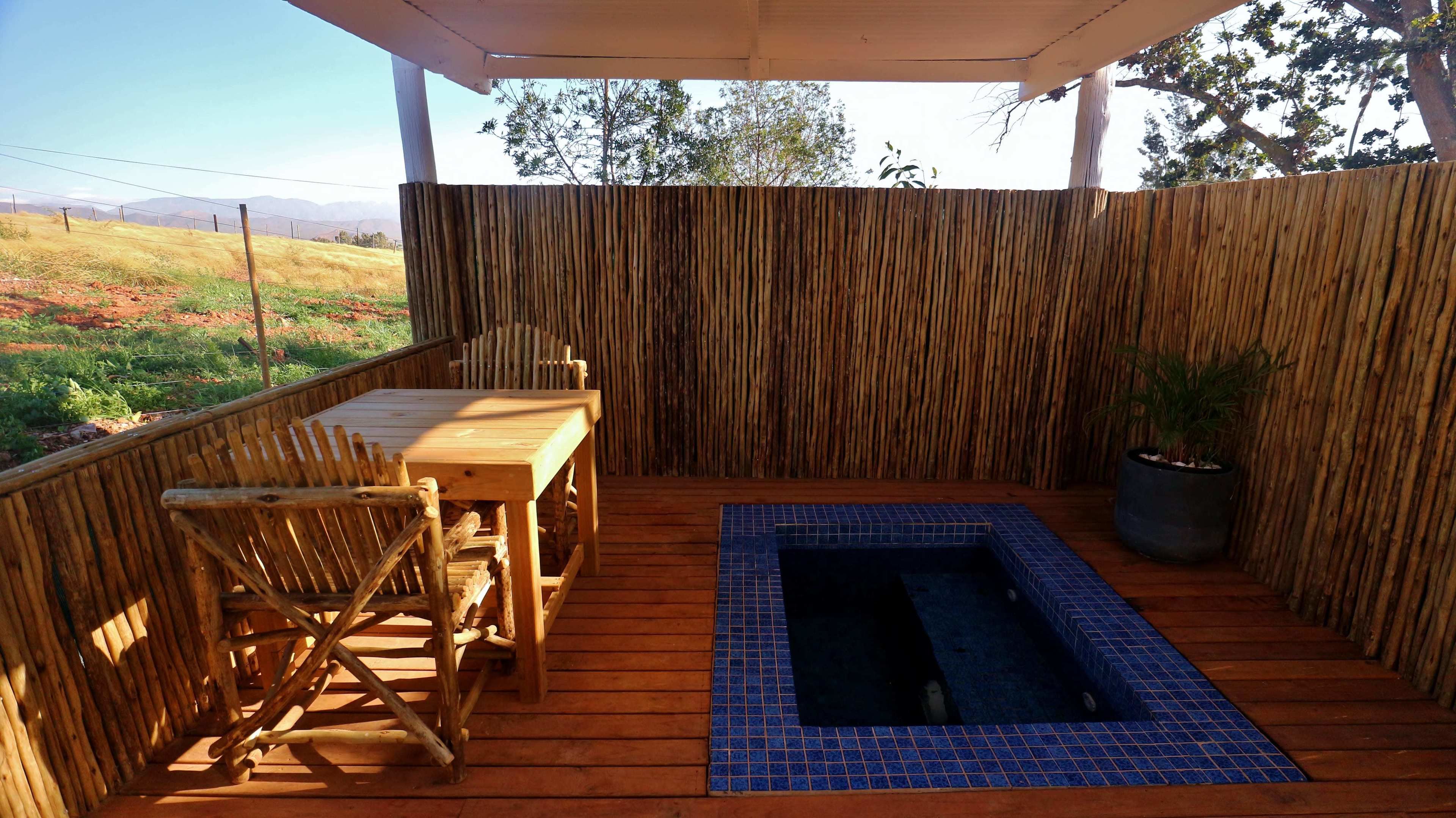 A wooden deck with a table and chairs, a small pool with blue tiles, and a bamboo fence.