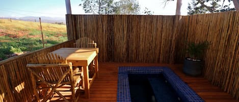 Een houten terras met een tafel en stoelen, een klein zwembad met blauwe tegels, en een bamboe hek.