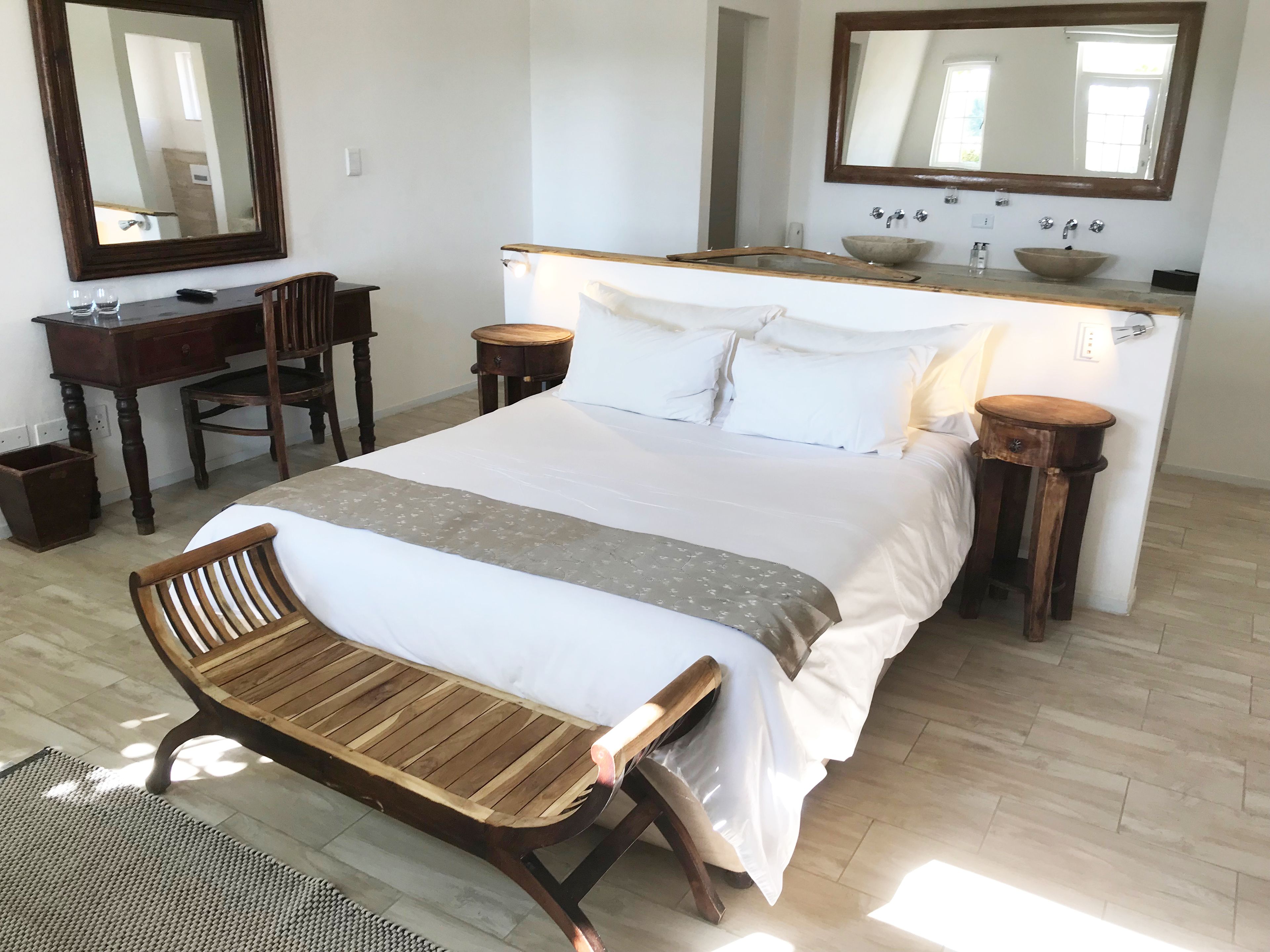 A bedroom with a bed, bedside tables, a wooden bench, a desk, and a large mirror.