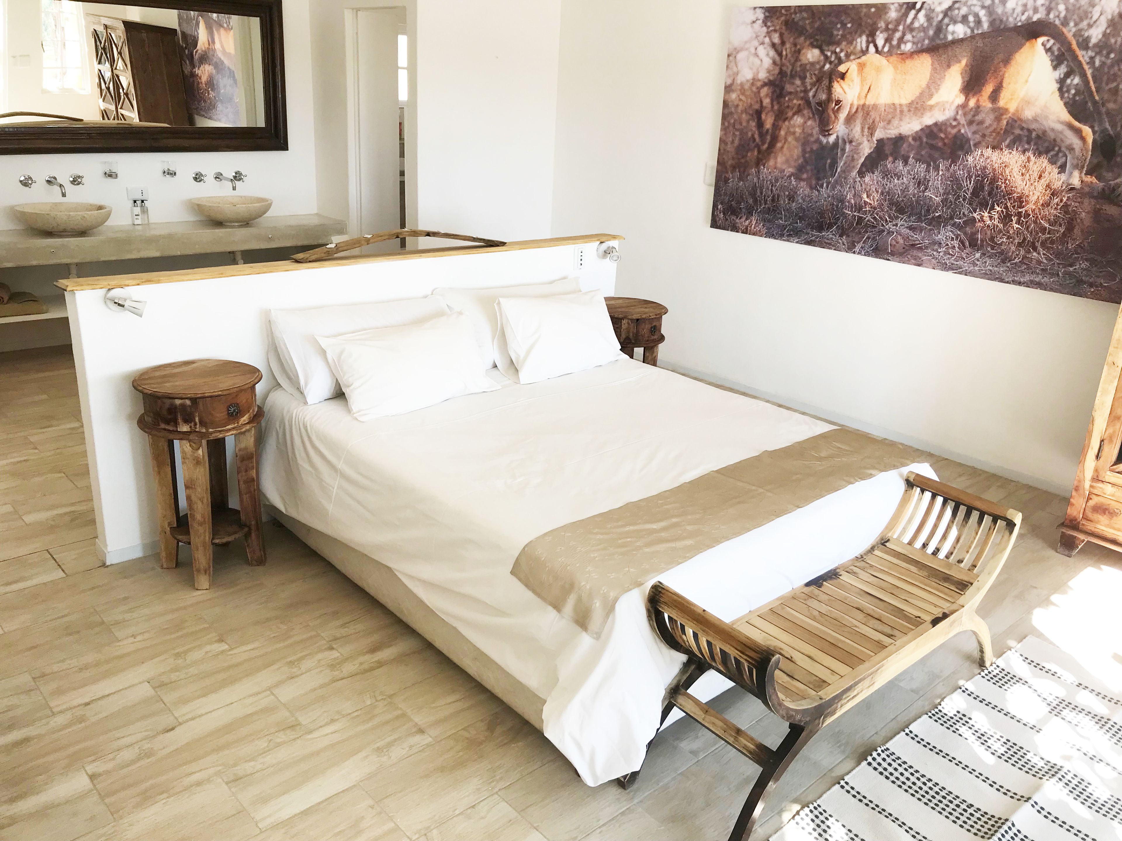 A bedroom with a bed, wooden nightstands, a wooden chair, a large mirror, and a painting of a lion.