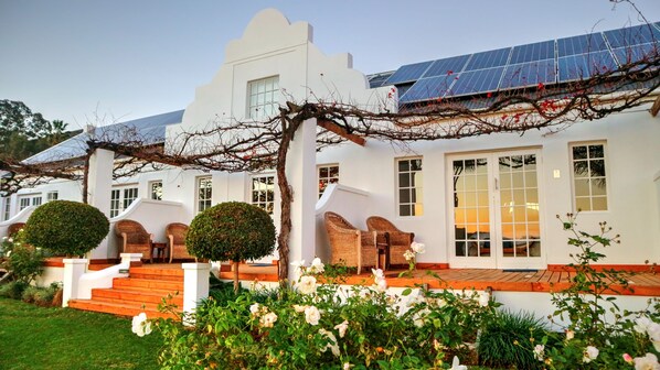 A white building with solar panels, a covered outdoor seating area, and a well-maintained garden.