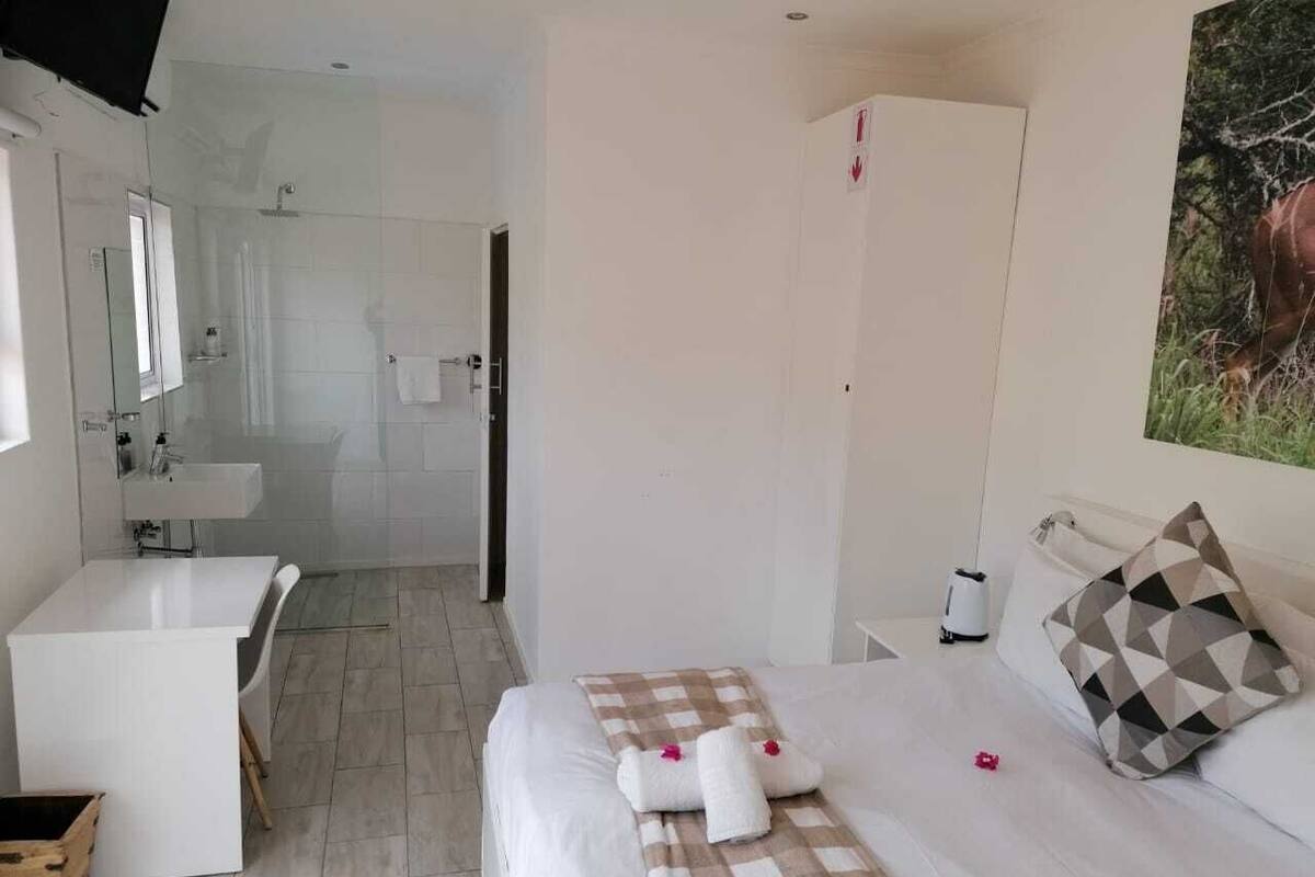 A hotel room with a bed, a bedside table, a mirror, a bathroom with a shower, and a sink.