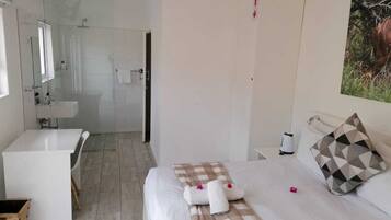 Habitación de hotel con cama, mesita de noche, espejo, baño con ducha y lavamanos.