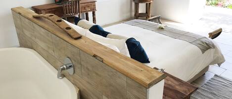A modern bathroom with a wooden vanity, a large sink, and a bed with a wooden headboard.