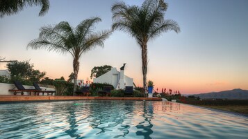 Piscina com espreguiçadeiras, palmeiras e um edifício moderno com design arquitetônico único.