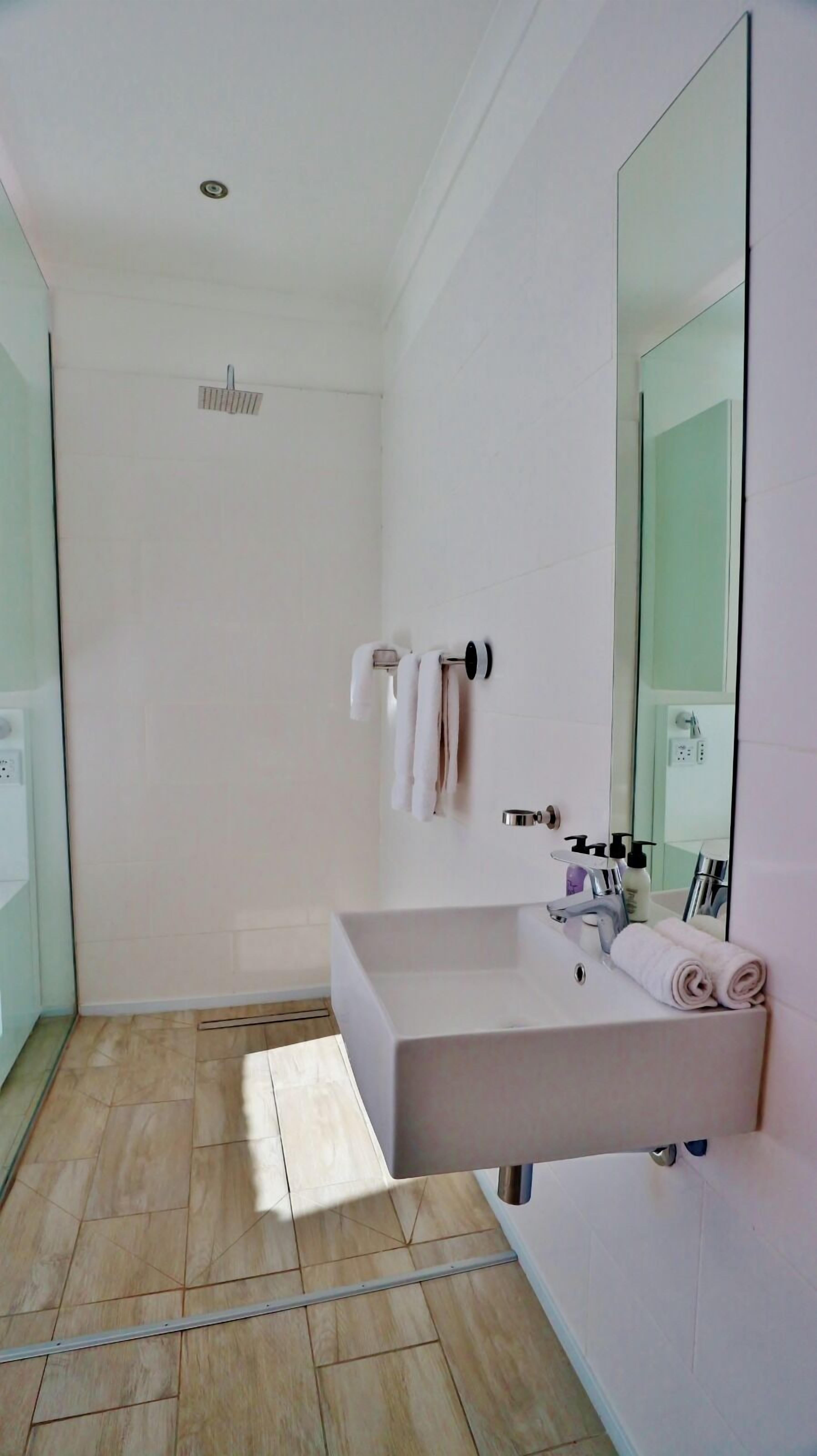 Un baño moderno con un espejo grande, un lavamanos rectangular y una zona de ducha.
