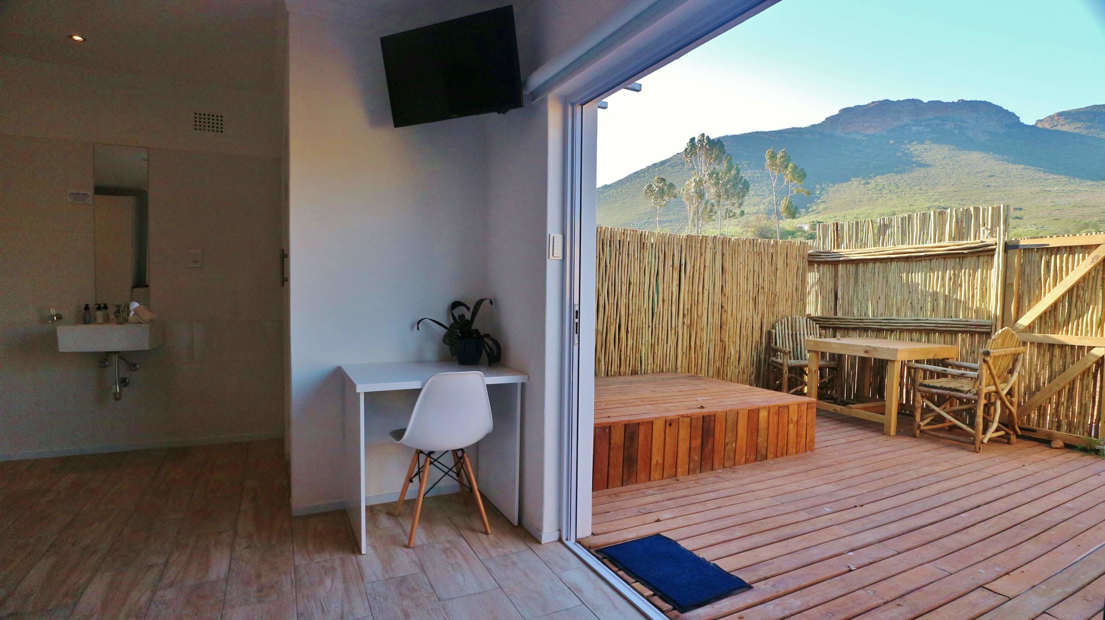 A room with a wooden desk, a white chair, a small bench, and a TV mounted on the wall.