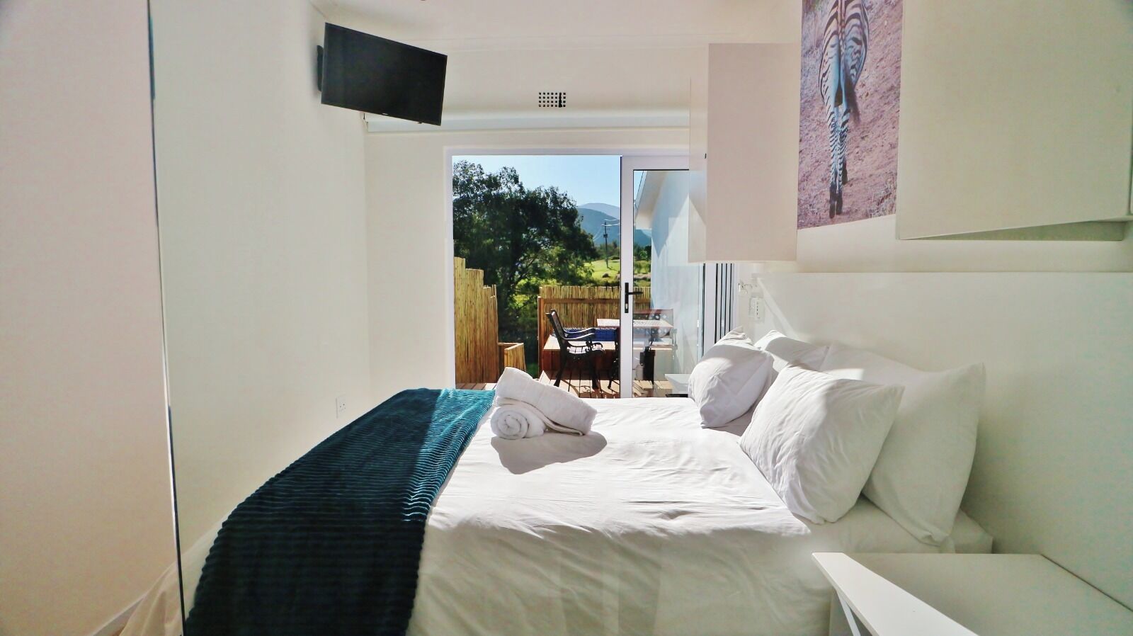 A hotel room with a bed, a TV mounted on the wall, and a view of the outside.
